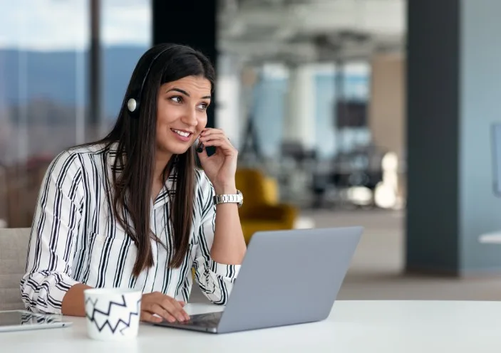 A woman sat at a desk adjusting the microphone of her headset during a call.