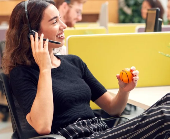 A woman at a table while holding a headset that's on her head.