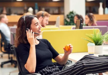 A woman at a table while holding a headset that's on her head.