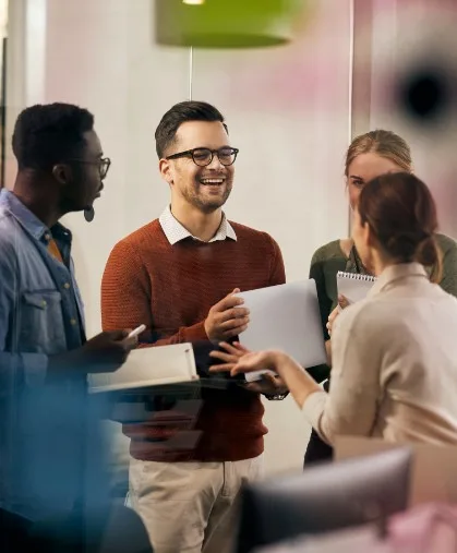 Four people who are standing in a circle talking and holding paper.
