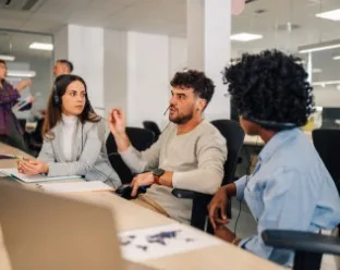 A group of people sat around a table with headsets on, the middle person is speaking.