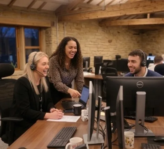 A close up of a desk at Parallel Partnerships during the late afternoon, three people are sat around the desk on a call.