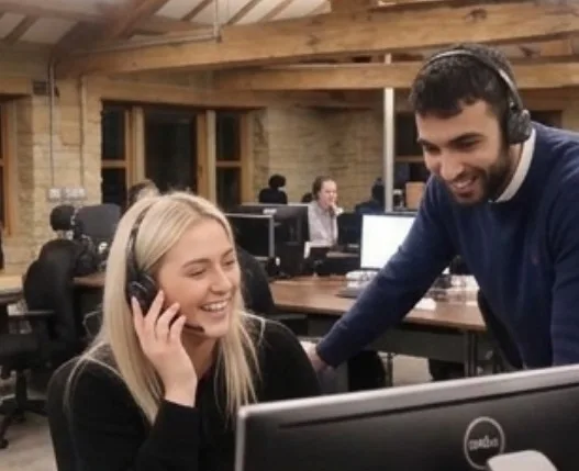 A call at Parallel Partnerships, two people are stood by a monitor with headsets on.