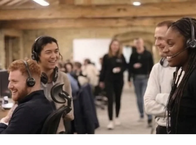 The Parallel Partnerships office with four people laughing in the foreground and the background is at a low depth of field so the rest of the office behind them is out of focus.